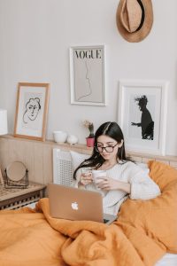 woman having coffee and using laptop in bed